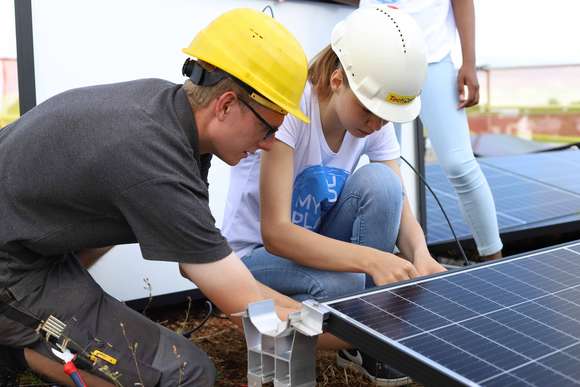 Nahaufnahme, dass einen Solarmonteur mit einer Schülerin bei der Montage eines Moduls zeigt.